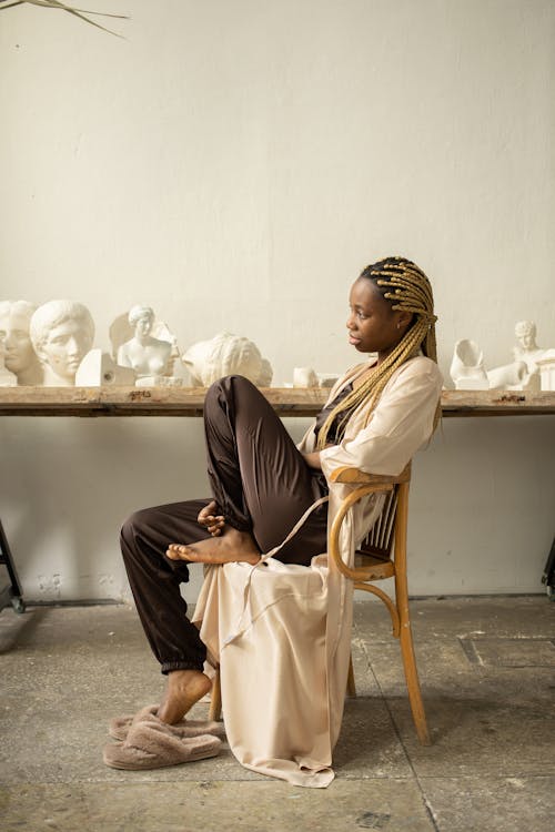 Photo of a Woman Sitting on a Chair Near Sculptures