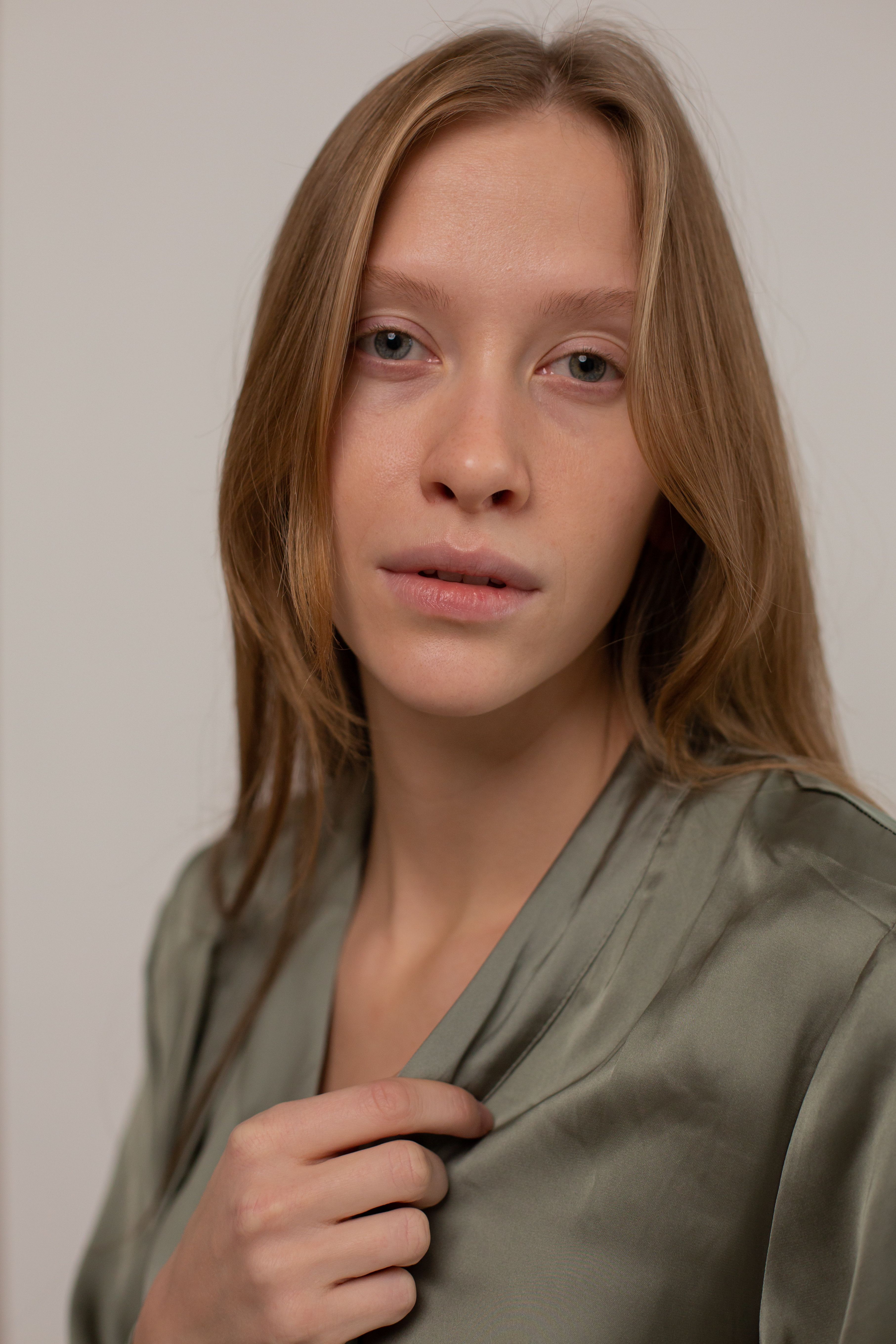 Close-up headshot of a young woman with long brown hair in a green silk robe, posing against a simple background.