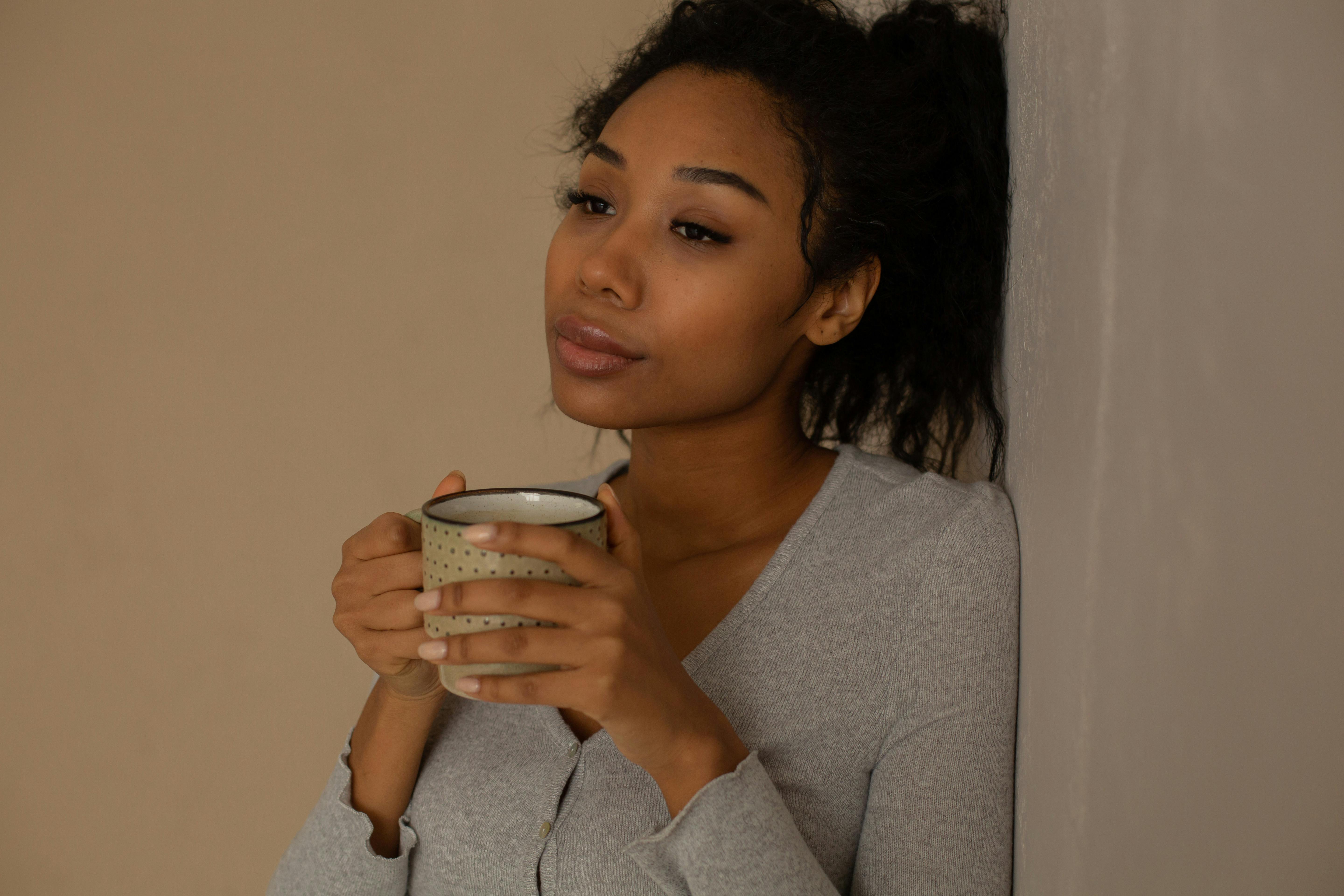 African American woman relaxing with a mug, leaning against a wall.