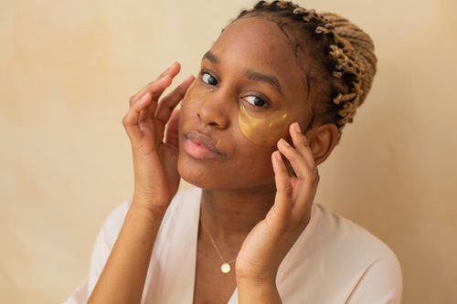 Free Portrait of an African American woman applying under-eye patches indoors. Stock Photo