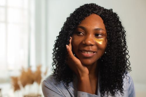 Free A smiling African American woman with curly hair enjoying her skincare routine indoors. Stock Photo