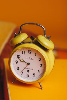 A classic yellow alarm clock with a retro style on a vivid orange background.