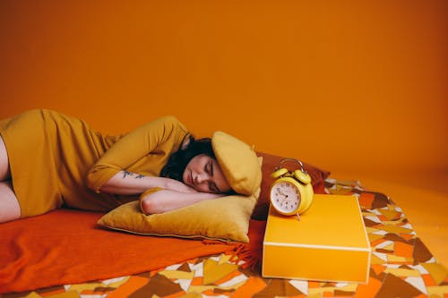 Photo Of Woman In Yellow Outfit Lying Down Beside An Alarm Clock