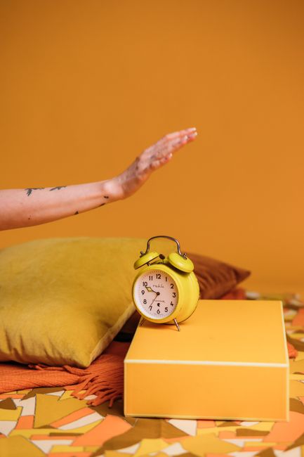 Stylish vintage yellow alarm clock on a colorful background with a woman's hand reaching for it.