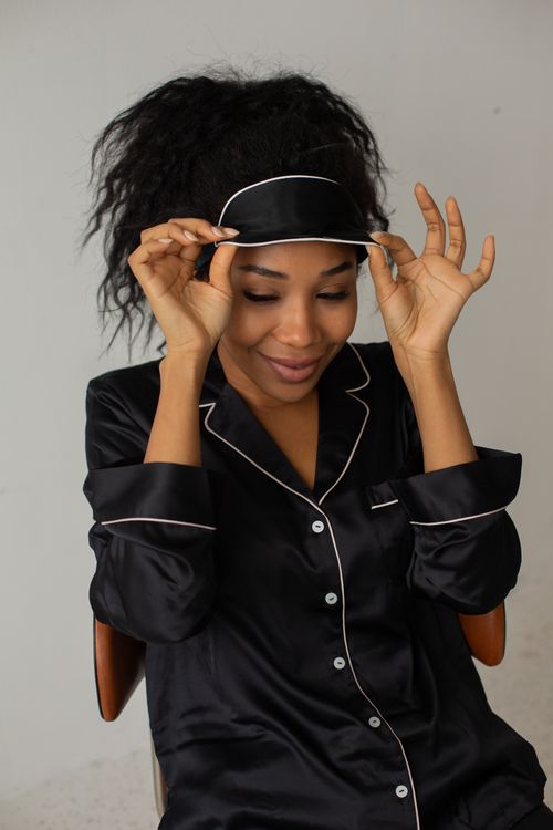 Free Portrait of a woman in black satin sleepwear adjusting a sleep mask, exuding comfort and relaxation. Stock Photo