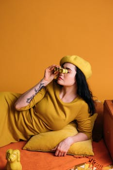Chic woman posing with binoculars against a vibrant yellow backdrop, symbolizing exploration.