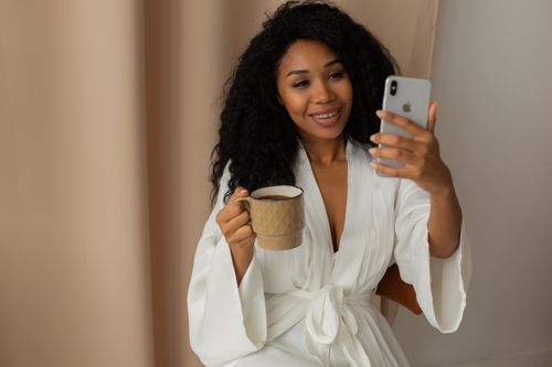 Free Relaxed woman in bathrobe holding coffee and smartphone indoors. Morning routine concept. Stock Photo