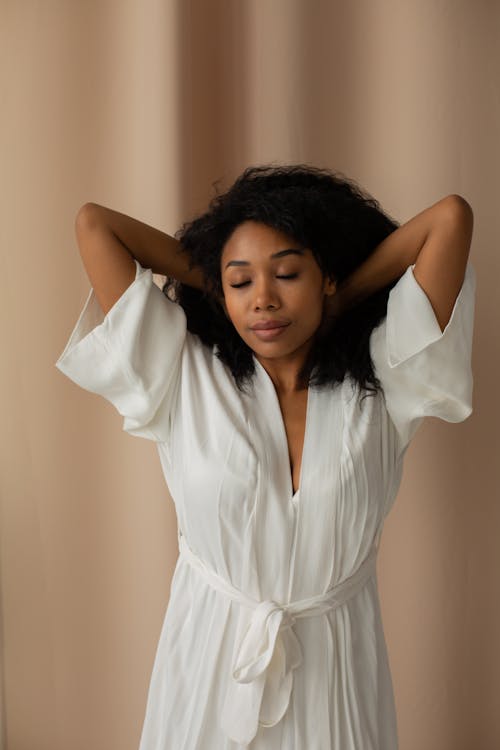 Free Woman Stretching Her Arms with Her Eyes Closed Wearing a White Dressing Gown  Stock Photo