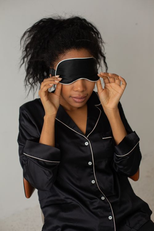 Free A woman wearing black satin pajamas adjusts her sleep mask indoors. Stock Photo