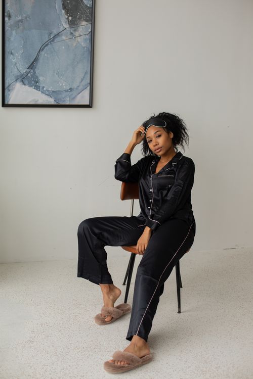 Free African American woman in black silk pajamas sitting indoors with a sleep mask. Stock Photo