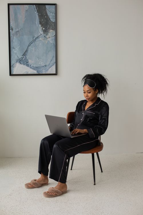 Free African American woman in pajamas using laptop, seated comfortably indoors. Stock Photo