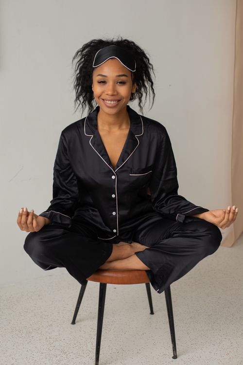 Free An African American woman smiling while meditating in silk pajamas on a chair indoors. Stock Photo