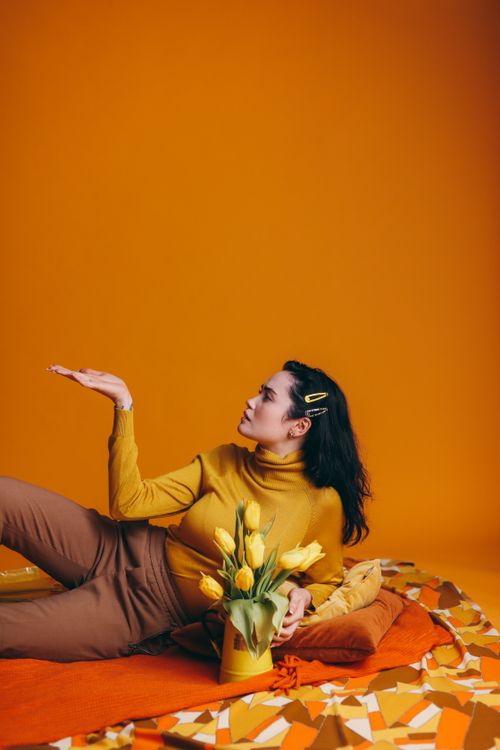 Free Stylish woman posing with yellow tulips on a vibrant yellow background. Stock Photo
