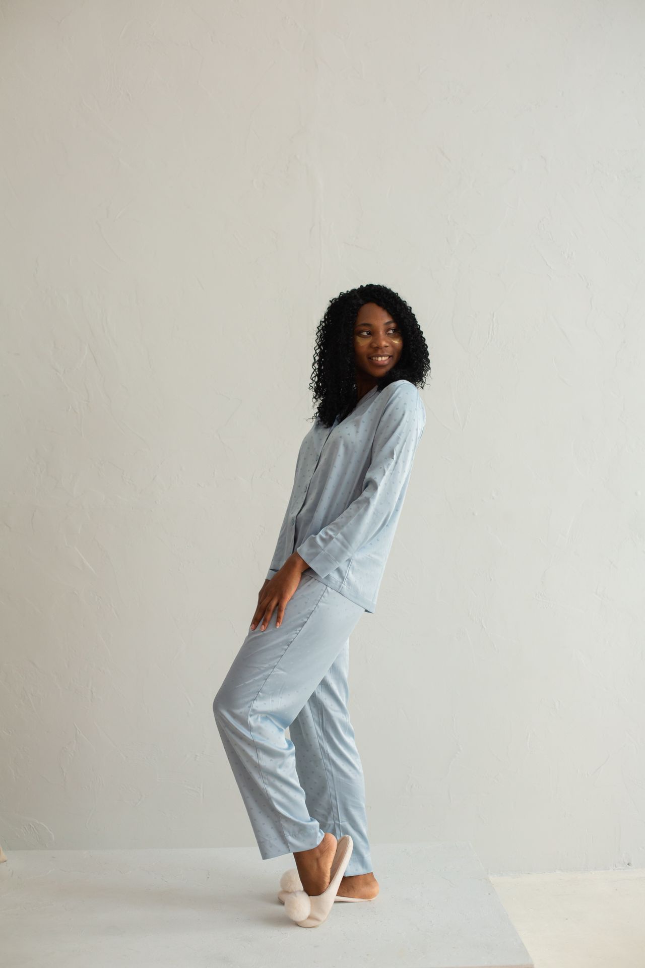 Woman in a light blue satin pajama set standing against a white wall