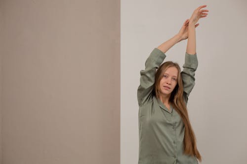 Free Woman Standing with Her Arms Stretched Upwards in a Pajama Shirt  Stock Photo