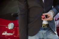 一名穿着西装的男子手拿骰子，站在一辆红色汽车旁，呈现出概念性和现代性的形象