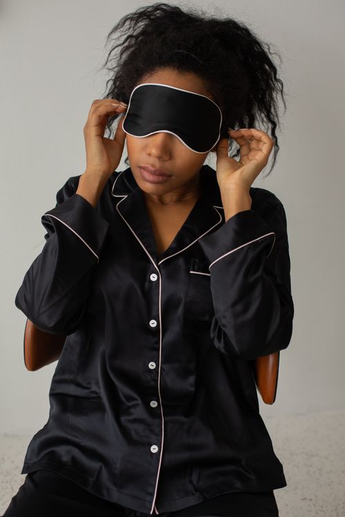 Free Woman in black satin pajamas adjusting a sleep mask indoors, promoting relaxation and comfort. Stock Photo