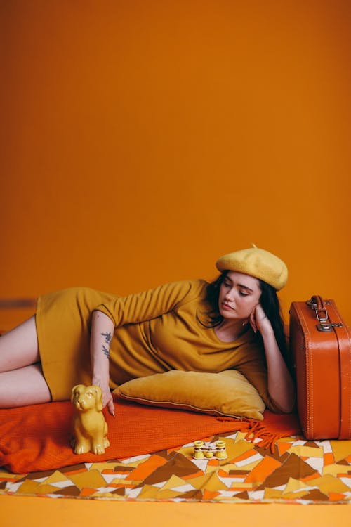 Free Woman in Yellow Long Sleeve Shirt and Brown Pants Lying on an Orange Color Textile Stock Photo