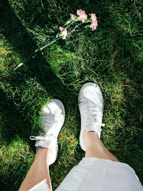 Free Overhead view of white sneakers on green grass with pink flowers, evoking a fresh spring vibe. Stock Photo