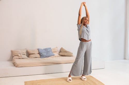 Free Woman in White Long Sleeve Shirt and White Pants Standing on Brown Wooden Bed Stock Photo