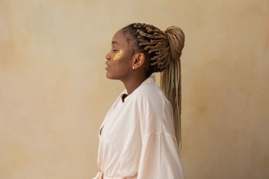 Profile view of a woman with golden skincare treatment on a neutral background.
