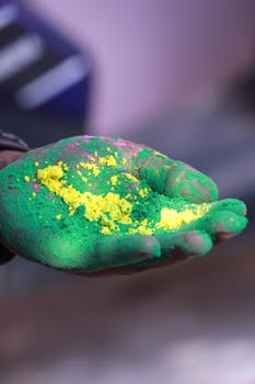 A hand holding vibrant green and yellow powders during Holi festival in Patna, India