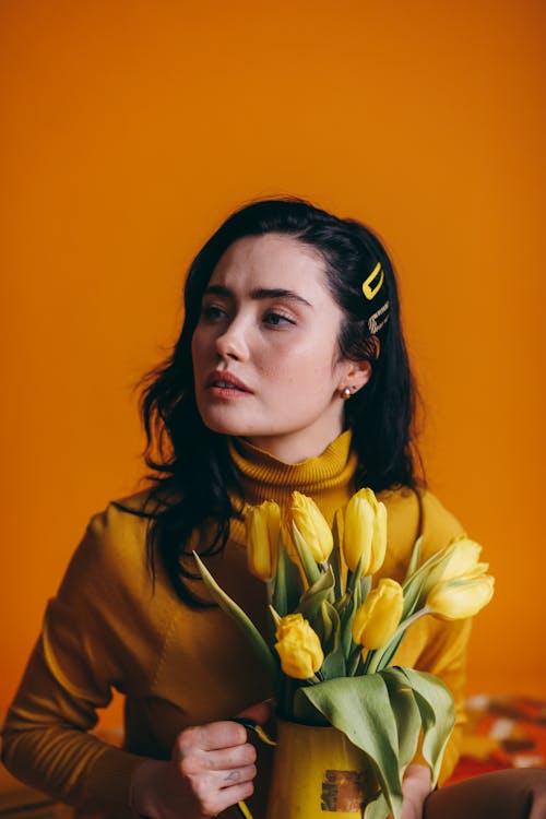 Free Woman in Brown Turtle Neck Shirt Holding Yellow Flowers Stock Photo