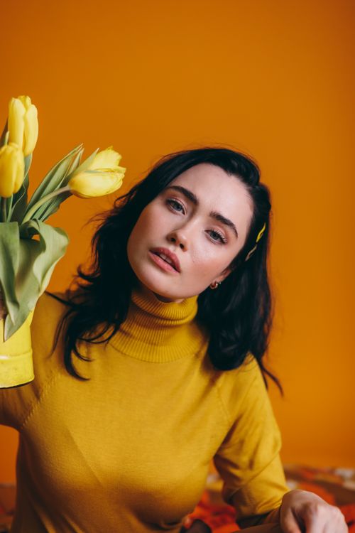 Free A fashionable woman with yellow tulips in a creative portrait against a vibrant background. Stock Photo