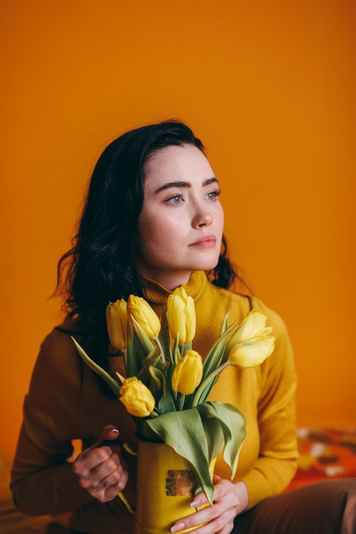 Free Fashionable portrait of a woman holding tulips against a bright yellow background. Stock Photo