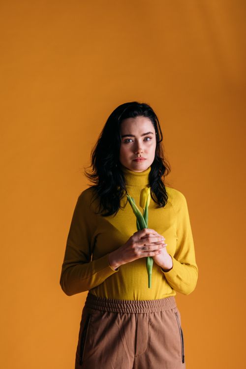 Free Stylish woman in yellow holding a tulip against a vibrant yellow background. Stock Photo