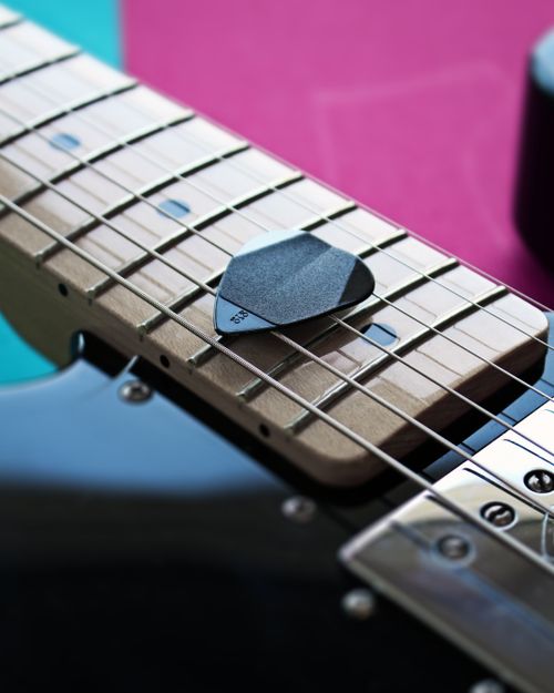 Free A black guitar pick resting on the strings of an electric guitar on a colorful background. Stock Photo