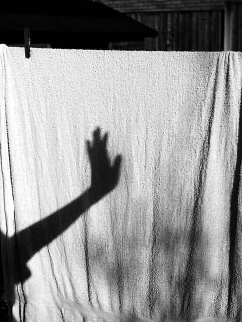 Artistic shadow of a hand cast on a sunlit towel outdoors, creating a dramatic silhouette.