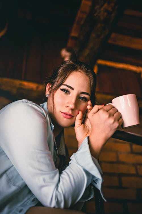 Free Young female with mug of hot aromatic coffee looking at camera on blurred background Stock Photo