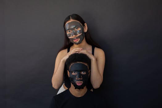 A diverse couple wearing skincare face masks posing against a black backdrop in a studio setting.