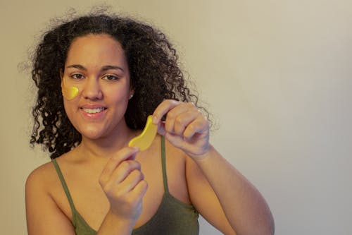 Optimistic ethnic female smiling widely while applying skincare patches for eyes and looking at camera