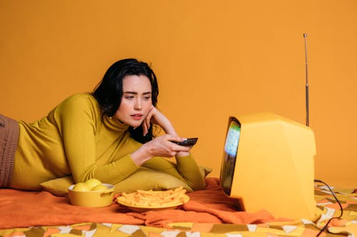 Woman in Yellow Long Sleeve Shirt Watching Tv In Bed