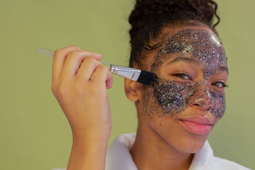 Smiling black woman spreading charcoal mask with brush