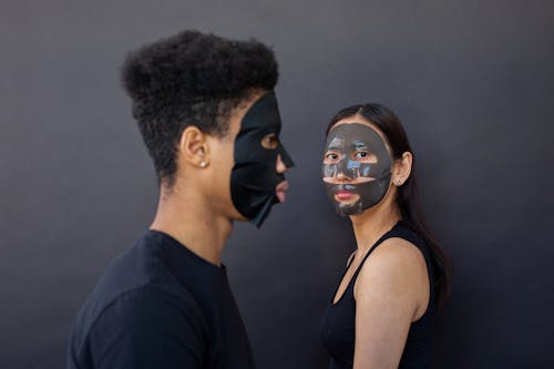 Free Side view of ethnic girlfriend in cleansing mask near African American boyfriend against black background Stock Photo