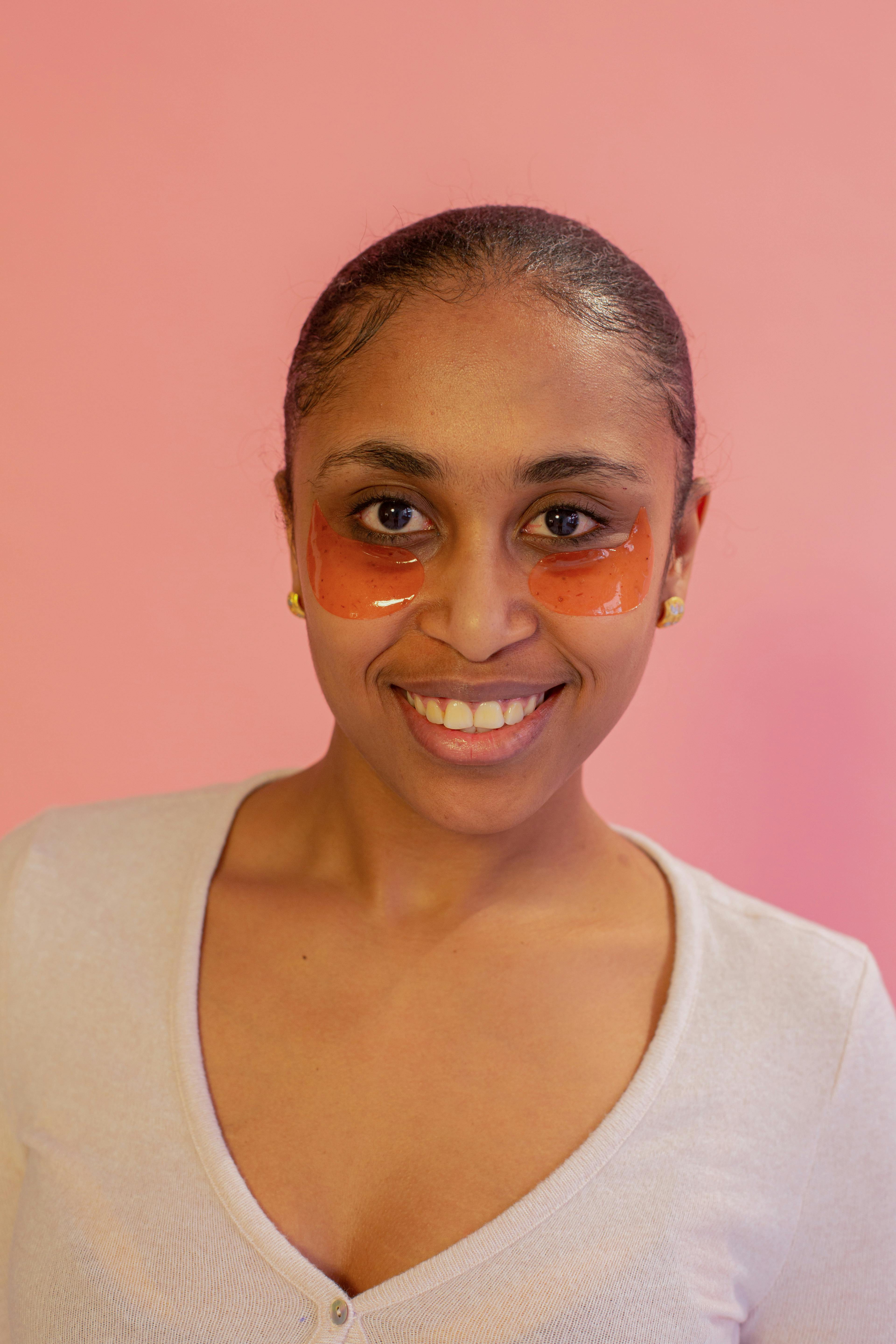 Young ethnic female in casual wear with eye patches on face looking at camera with toothy smile