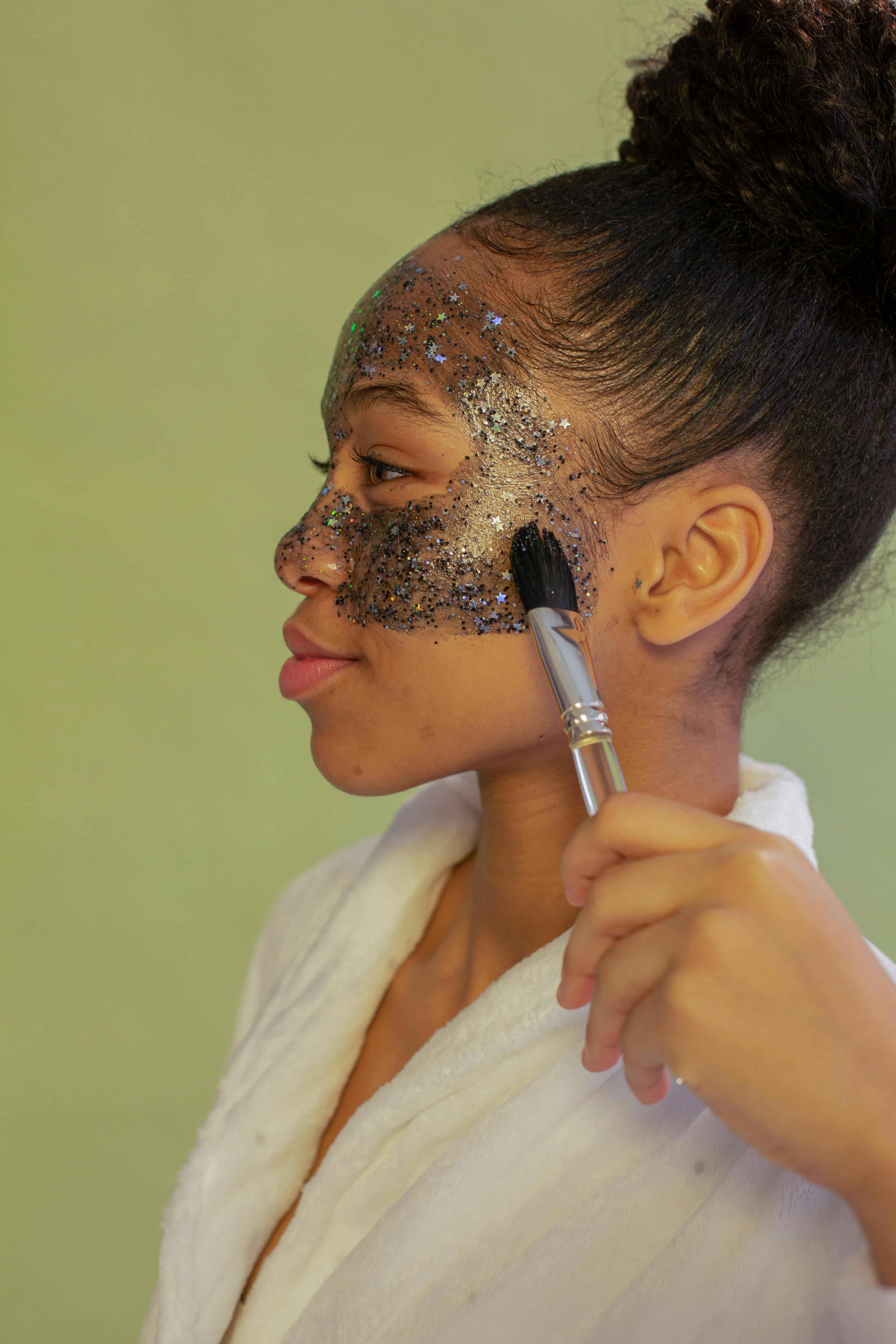 black teen applying exfoliating mask on face on green background