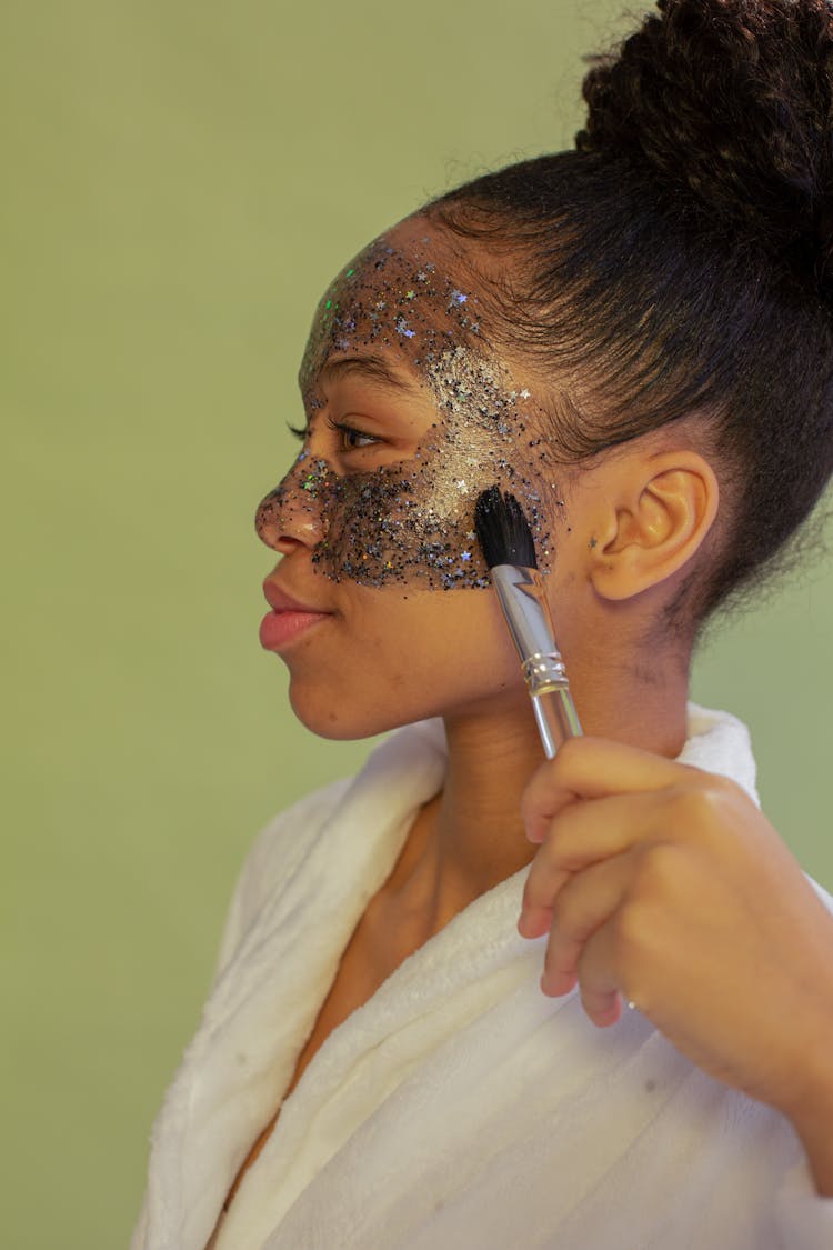 Black Teen Applying Exfoliating Mask On Face On Green Background