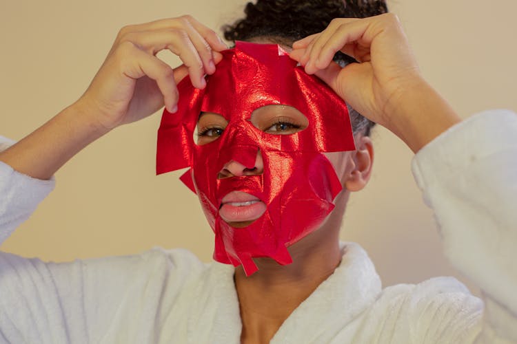 Black Woman Applying Moisturizing Red Mask On Face