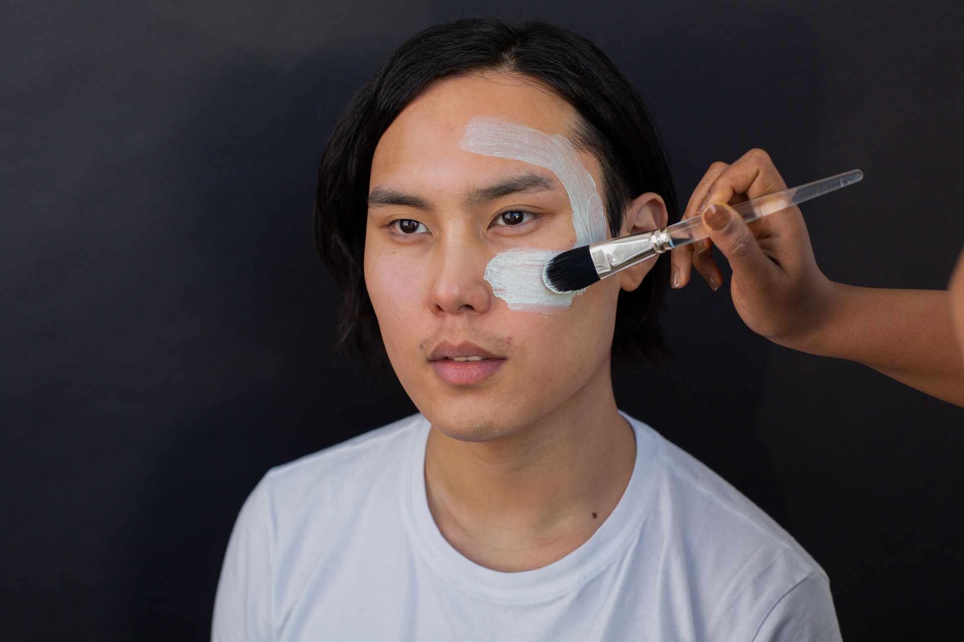 Crop beautician applying mask on face of Asian client