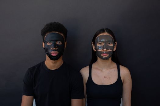 Young black man with Asian female partner with cleansing masks on faces looking at camera