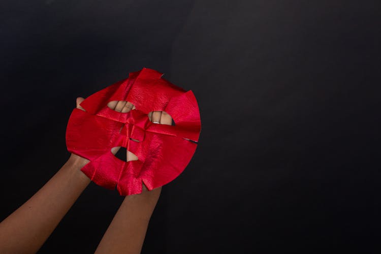 Crop Person Showing Red Sheet Mask On Black Background