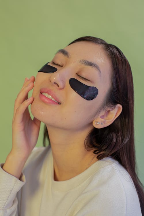 Free Young gentle ethnic female with closed eyes and eye patches touching face with delicate skin Stock Photo