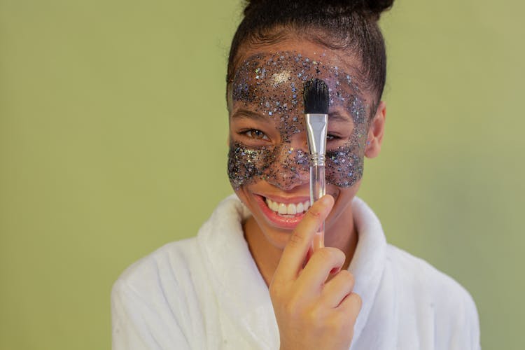 Happy Black Teen Applying Exfoliating Mask On Face With Applicator
