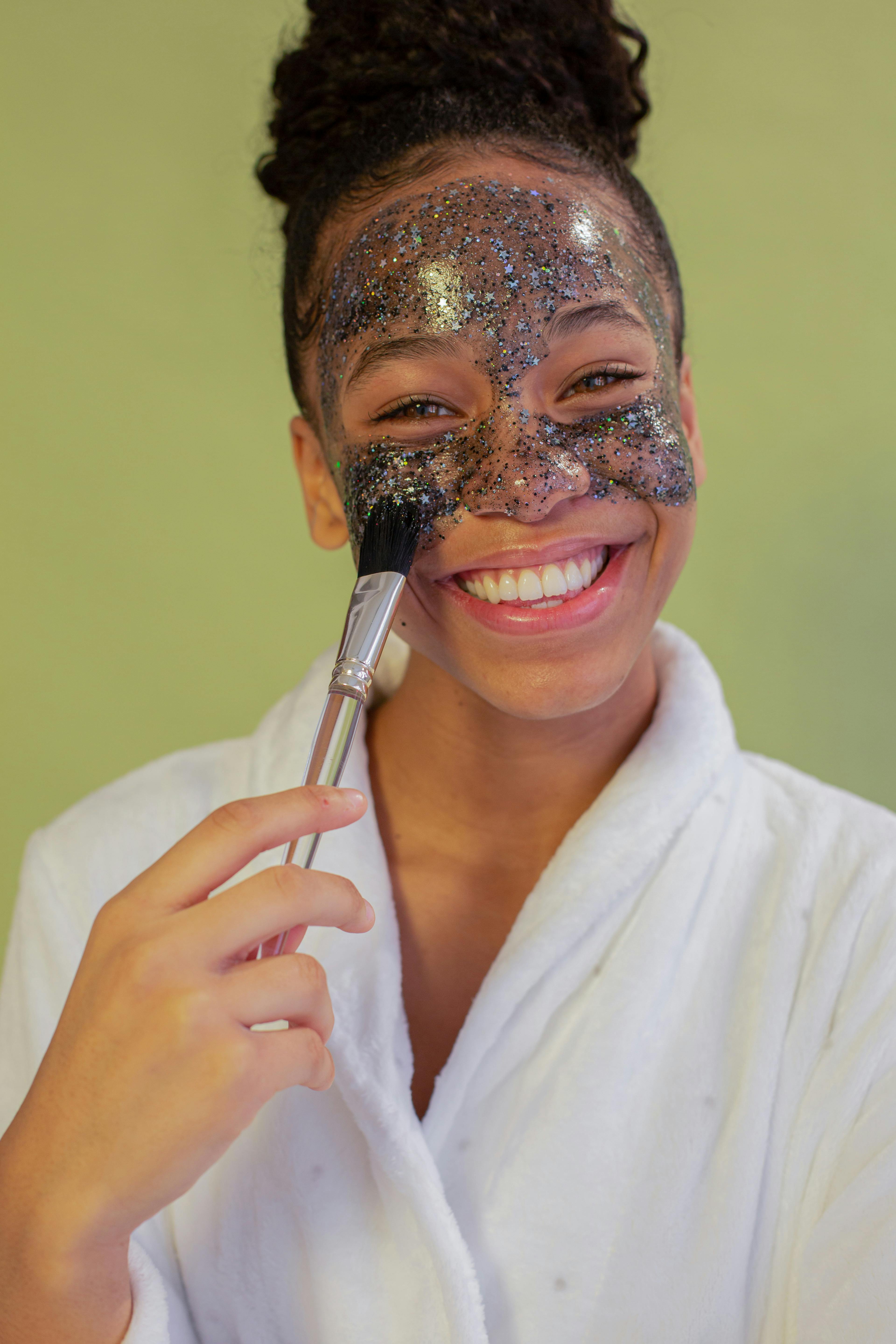 happy black teenager applying glitter face mask on face