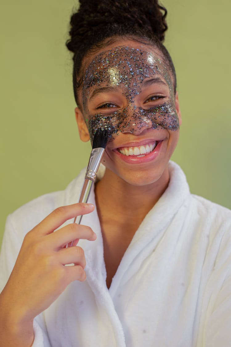 Happy Black Teenager Applying Glitter Face Mask On Face