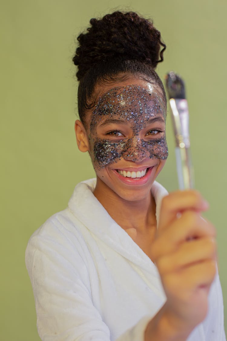 Cheerful Black Teenager With Applicator And Glitter Mask On Face